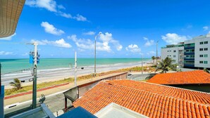 A coastal view with a beach, a road, and a building with a red-tiled roof.