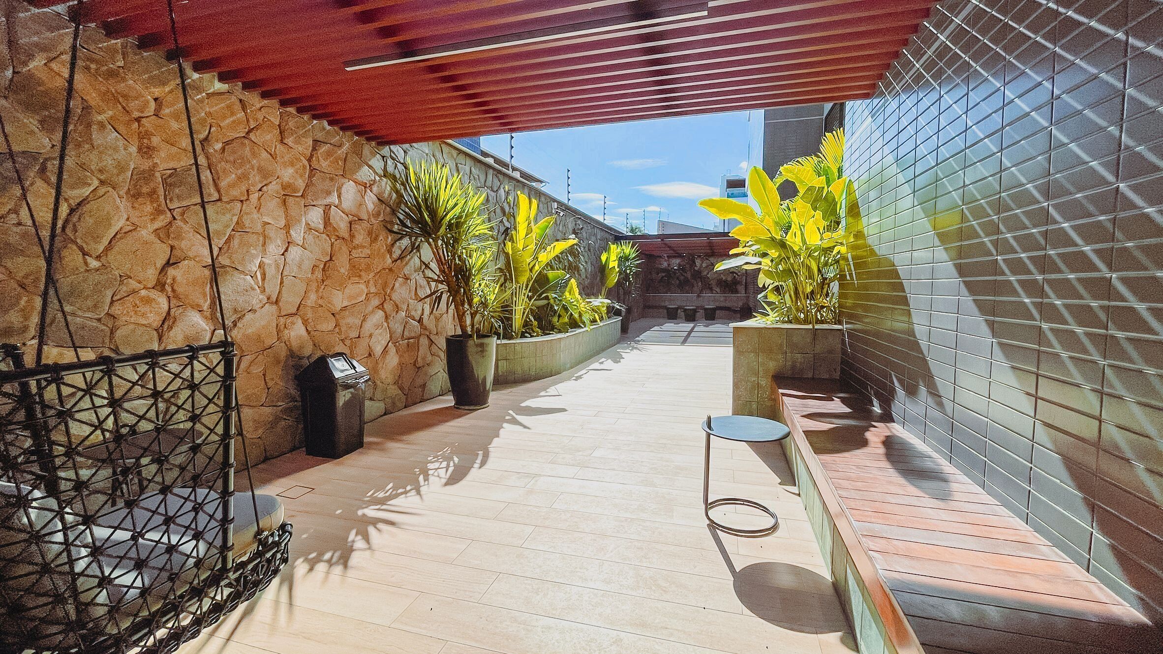 A narrow outdoor corridor with a stone wall on one side, a tiled wall on the other, and a wooden bench along the right.