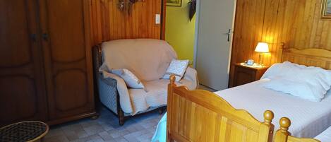 Una habitación con paneles de madera, una cama, una silla, una mesita y una puerta.