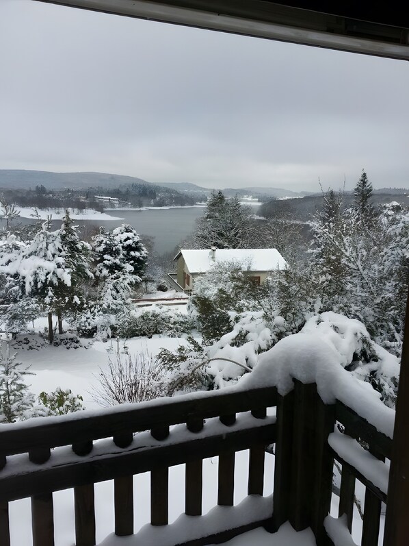 A snowy landscape with a lake, trees, and a building in the distance.