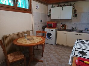 A kitchen with a table, chairs, a washing machine, a microwave, a stove, and cabinets.