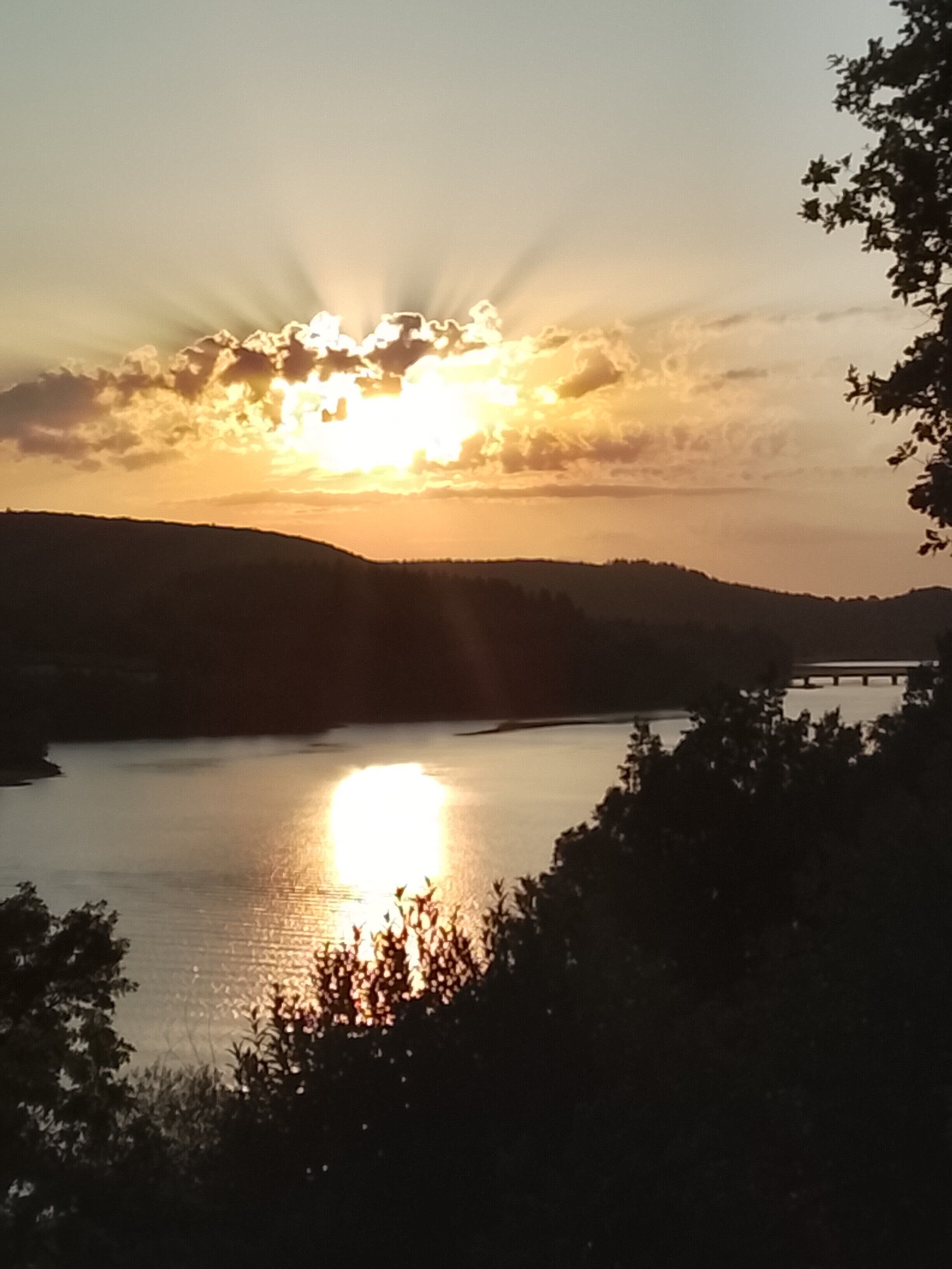 Un coucher de soleil sur une étendue d’eau calme, avec la silhouette de collines en arrière-plan.