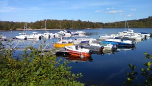 Ein Yachthafen mit verschiedenen Schiffen, umgeben von ruhigem Wasser und einer bewaldeten Uferlinie.