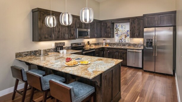 A modern kitchen with dark wood cabinets, stainless steel appliances, and a granite island with bar stools. - St George | Elevated Red Rock Retreat | Pool + Hot Tub | 3BR Sleeps 6 (St. George)