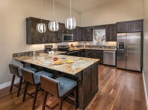 Una cocina moderna con armarios de madera oscura, electrodomésticos de acero inoxidable y una isla de granito con taburetes de bar.