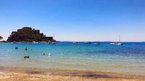 A beach with clear blue water, boats, and a small island with buildings. - ZEcamping 4 étoiles espace aquatique locatif TV 24m2 4 pers (Hyères)