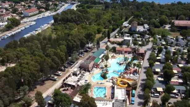 An aerial view of a coastal resort with a central swimming pool, a water slide, and a marina with boats. - ZEcamping 4 étoiles espace aquatique locatif TV 24m2 4 pers (Hyères)
