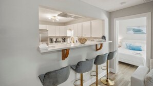 Una cocina moderna con armarios blancos, una encimera blanca y un espejo grande sobre los taburetes de bar.