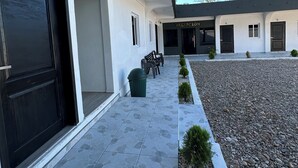 A modern building with a covered walkway, numbered doors, and a gravel area with small plants.