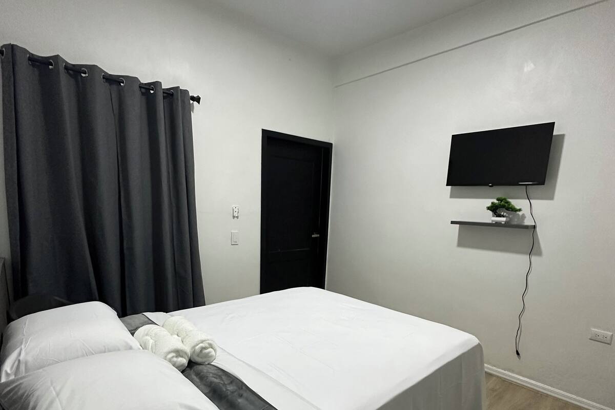 Un dormitorio con una cama, televisor montado en la pared y una puerta.