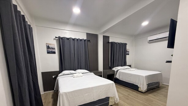 A hotel room with two beds, dark curtains, a white wall, and a wooden floor.