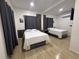 Una habitación de hotel con dos camas, cortinas oscuras, una pared blanca y suelo de madera.