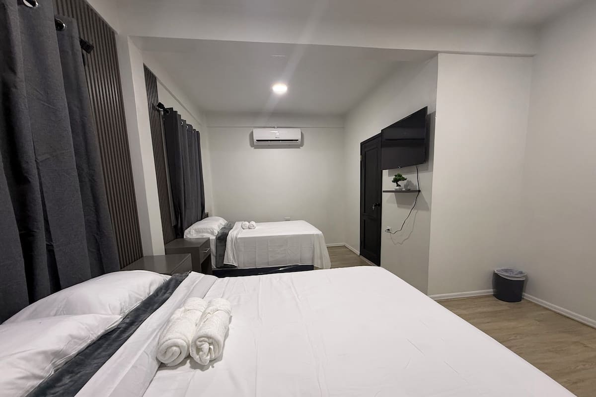 Habitación de hotel con cama, escritorio, silla, una mesita pequeña, unidad de aire acondicionado y un cubo de basura.