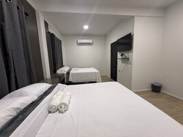 Habitación de hotel con cama, escritorio, silla, una mesita pequeña, unidad de aire acondicionado y un cubo de basura.