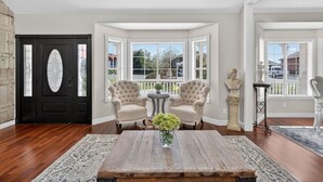 A room with a dark wooden door, two upholstered armchairs, a round wooden coffee table, and a vase with flowers. - 4BR Home | Pool, Hot Tub, Game Room & Fire Pit (Mesa)
