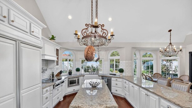 A spacious kitchen with white cabinetry, granite countertops, a central island, and two chandeliers. - 4BR Home | Pool, Hot Tub, Game Room & Fire Pit (Mesa)