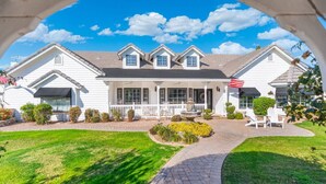A two-story house with a porch, a flag, and a well-maintained lawn. - 4BR Home | Pool, Hot Tub, Game Room & Fire Pit (Mesa)