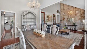 A spacious dining area with a wooden table, white chairs, and a chandelier. - 4BR Home | Pool, Hot Tub, Game Room & Fire Pit (Mesa)