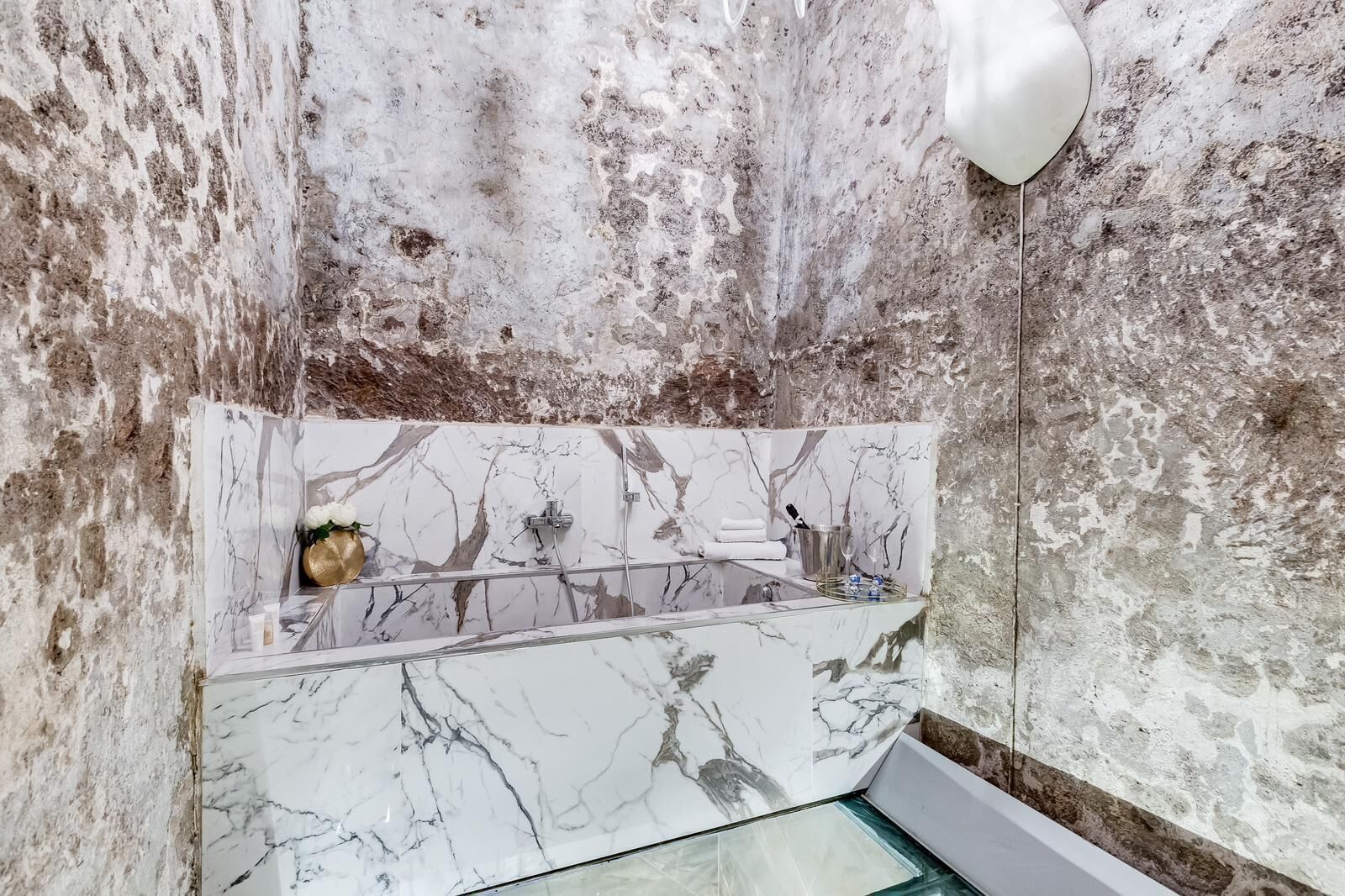 A bathroom with a marble sink, a glass shower enclosure, and a textured wall.