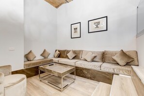 Uma sala de estar moderna com um sofá bege, uma mesa de centro de vidro e piso de madeira.