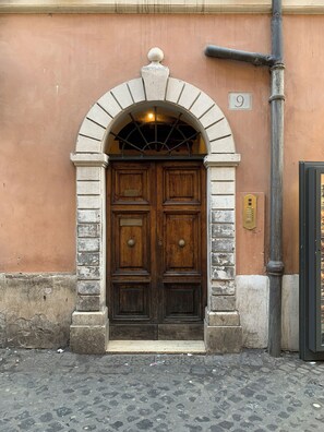 Une porte en bois à deux battants, surmontée d’un arc en pierre, avec une plaque en laiton et un panneau portant le chiffre « 9 » sur la façade d’un immeuble.