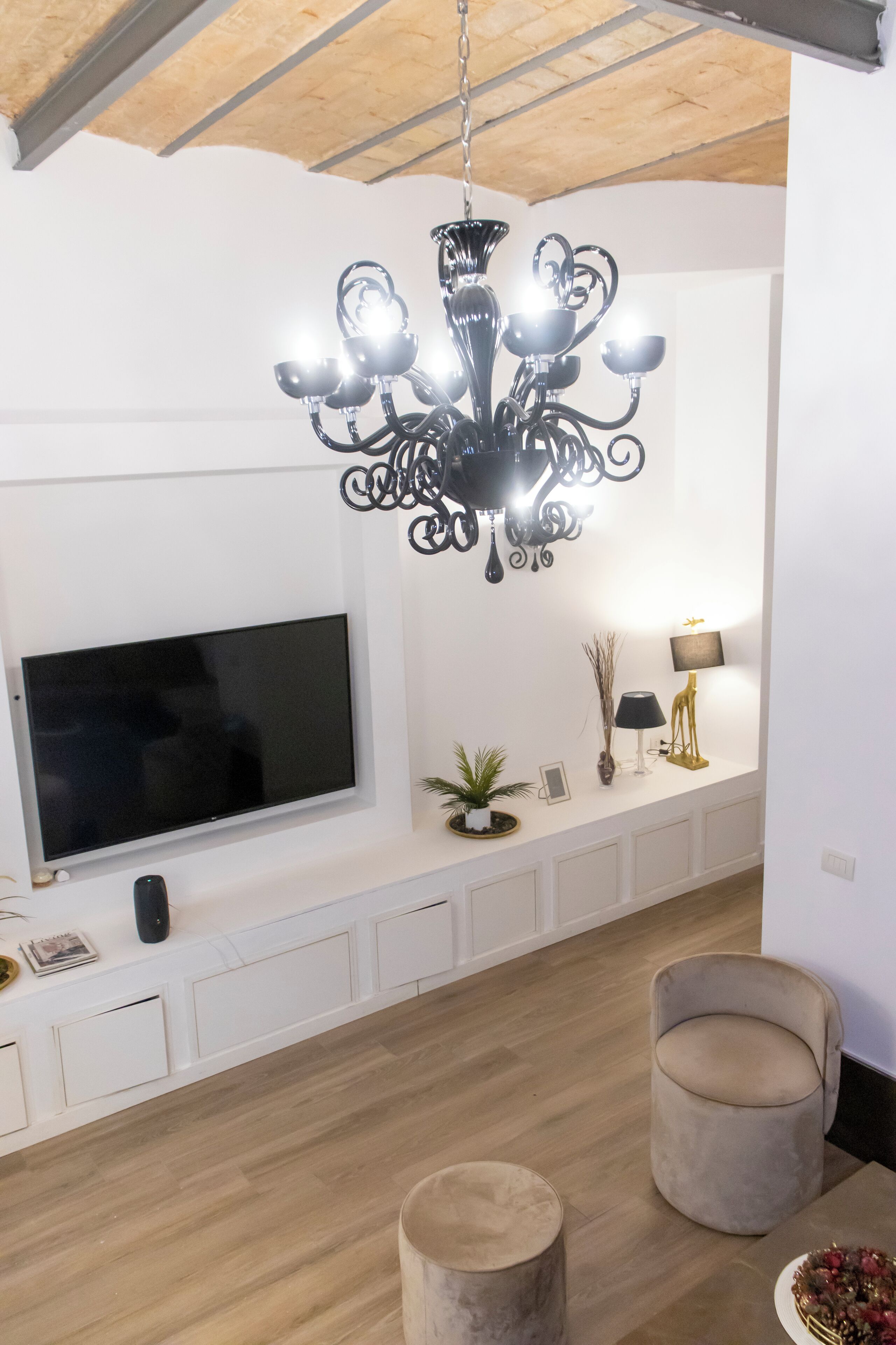 A modern living room with a flat-screen TV, a chandelier, and two armchairs.