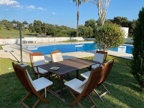 Un espace aménagé au bord de la piscine, avec une table et des chaises, une piscine et de la verdure tout autour.