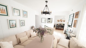 Ein modernes Wohnzimmer mit einer beigefarbenen Sofagarnitur, einem Esstisch mit Blumenvase und gerahmten Bildern an den Wänden.
