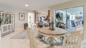 A dining area with a round table, white chairs, and a kitchen in the background. - Sunset Reach ...Waterfront Family Pool Home - Gulf Access -  Sunset Views - (Cape Coral)