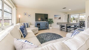 A spacious living room with a large sofa, a TV, and a dining area. - Sunset Reach ...Waterfront Family Pool Home - Gulf Access -  Sunset Views - (Cape Coral)