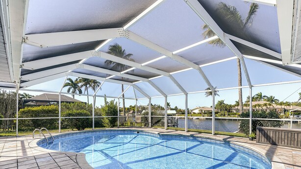 A covered swimming pool with a view of a lake and palm trees. - Sunset Reach ...Waterfront Family Pool Home - Gulf Access -  Sunset Views - (Cape Coral)