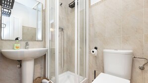 Et badeværelse med en glasafskærmet brusekabine, et konsolbord med vask og et toilet.