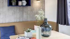 A modern living room with a wooden table, a blue sofa, and a wall-mounted shelf with decorative items. - ZEcamping 4 étoiles 200m plage piscine couverte locatif TV LV BBQ 35m2 (Névez)