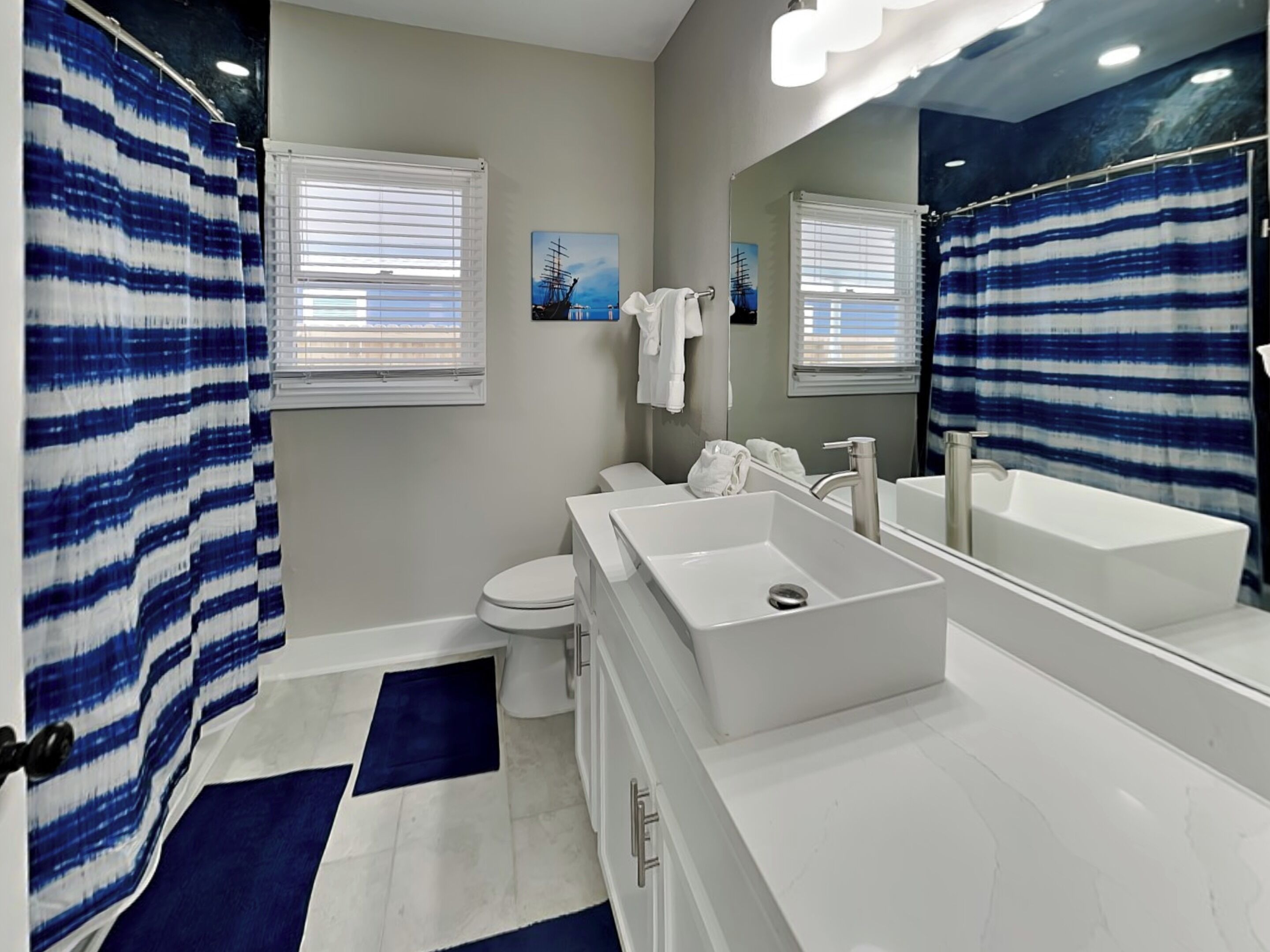 A modern bathroom with a large mirror, a bathtub, a toilet, and a sink.