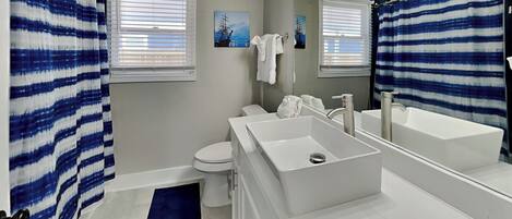 A modern bathroom with a large mirror, a bathtub, a toilet, and a sink.