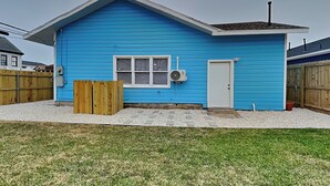 Une maison bleue d’un seul étage, avec une porte blanche, une fenêtre et un petit garage attenant.