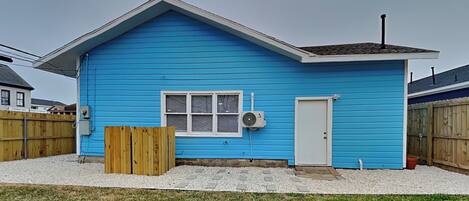 Une maison bleue d’un seul étage, avec une porte blanche, une fenêtre et un petit garage attenant.