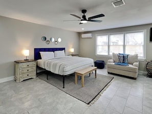 A bedroom with a bed, bedside tables, a ceiling fan, a window, a sofa, and a rug. - Blue Oasis Retreat (Galveston)