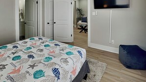 Quarto com cama, televisão fixada na parede e porta que dá para outro cômodo.