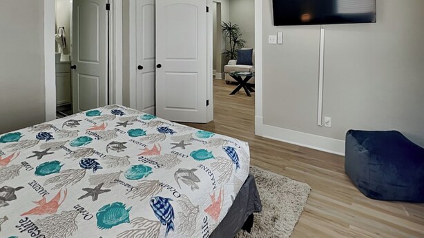 Une chambre à coucher avec un lit, un téléviseur fixé au mur et une porte donnant sur une autre pièce.