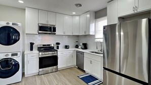 Uma cozinha moderna com armários brancos, eletrodomésticos de aço inoxidável, forno embutido, micro-ondas e geladeira.