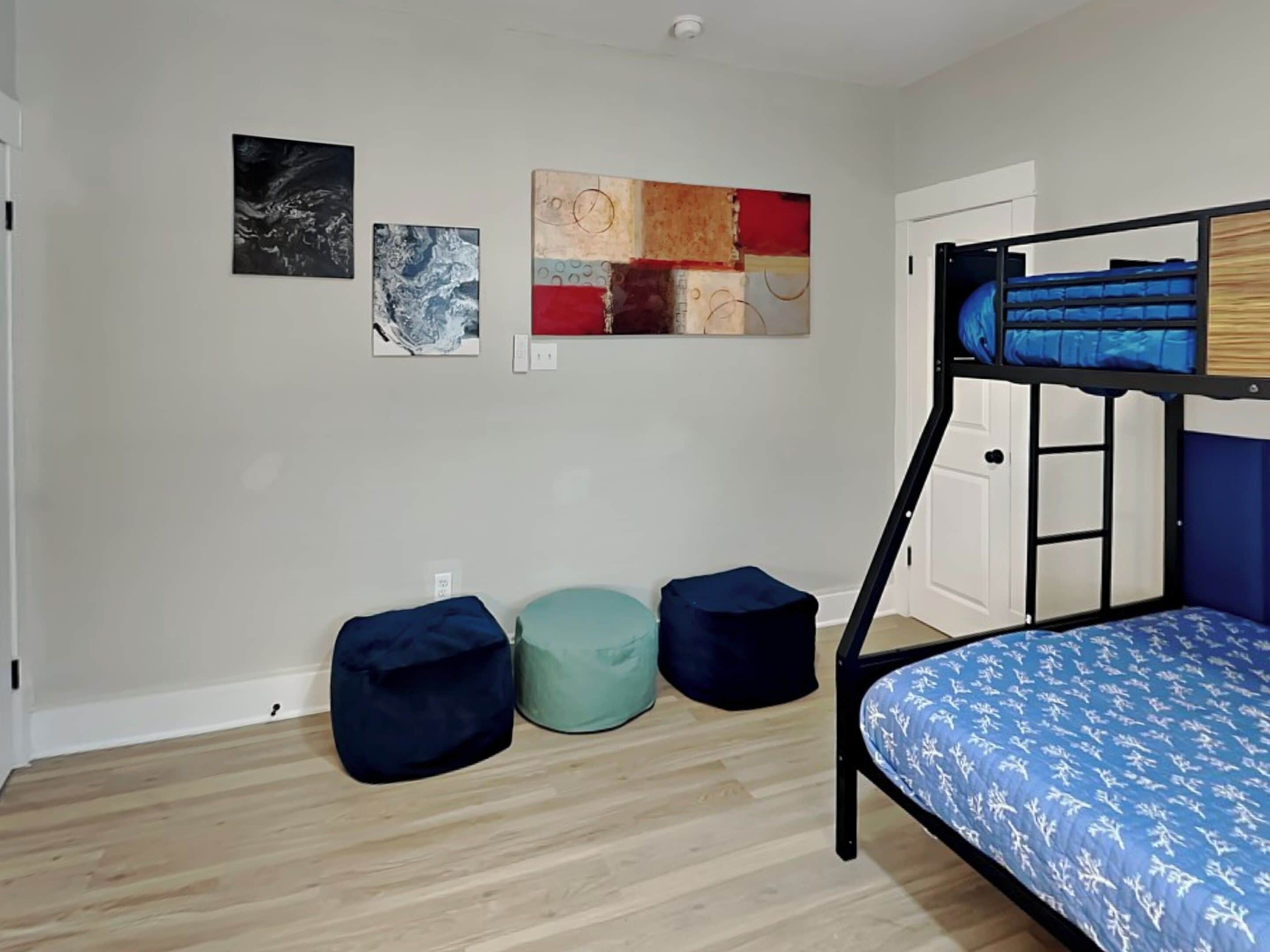 A room with a bunk bed, three bean bags, and three artworks on the wall.