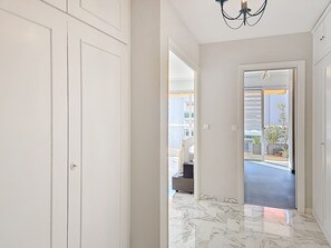 Ein Flur mit weißen Türen, einer Chandelüster und Blick auf einen Balkon mit Pflanzen.