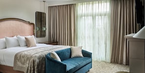 A hotel room with a large bed, a blue armchair, a wooden headboard, a nightstand, a mirror, and a large window with curtains. - Mirbeau Inn & Spa Beacon (Beacon)