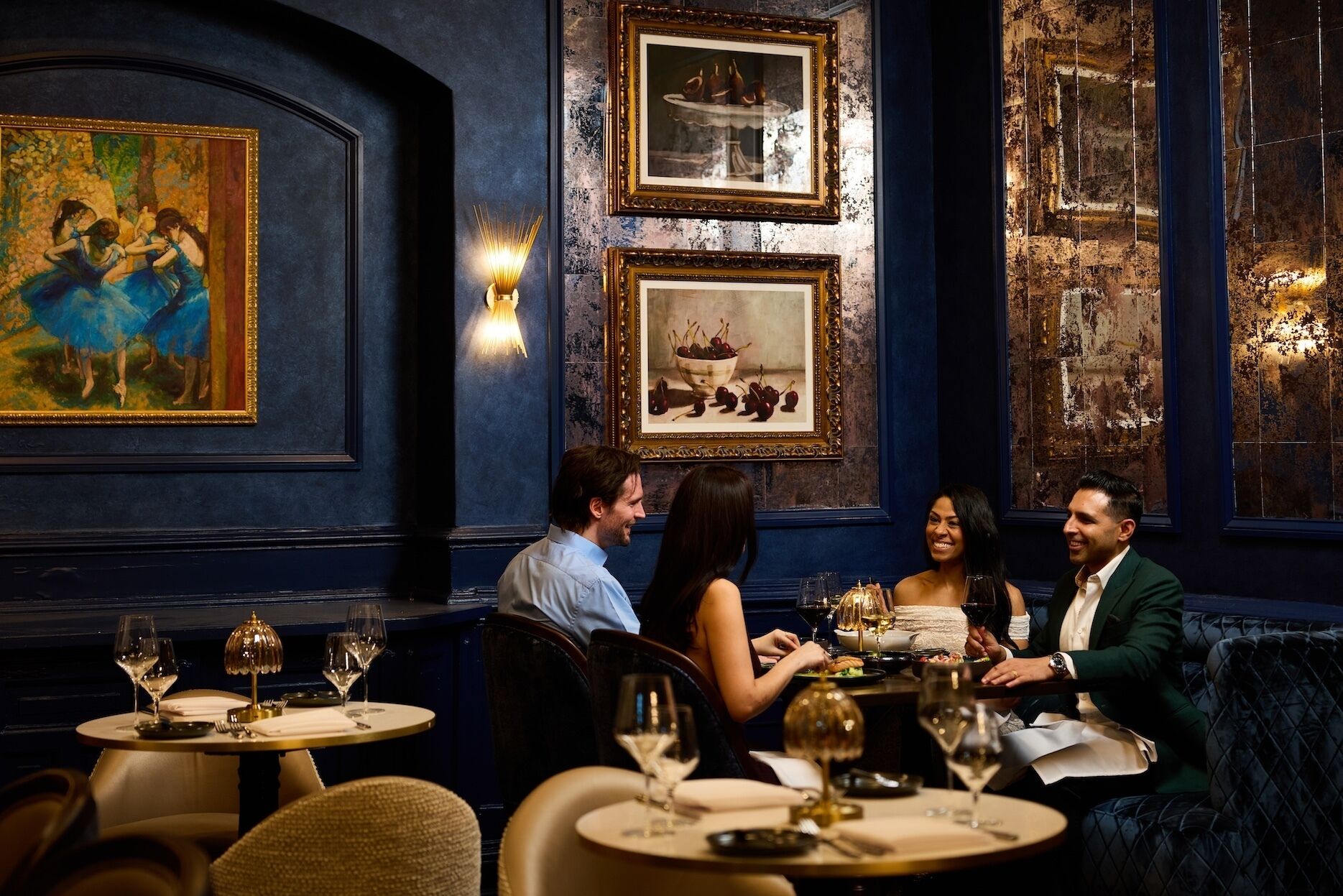 A restaurant with round tables, framed artwork on the walls, and a dark blue interior.