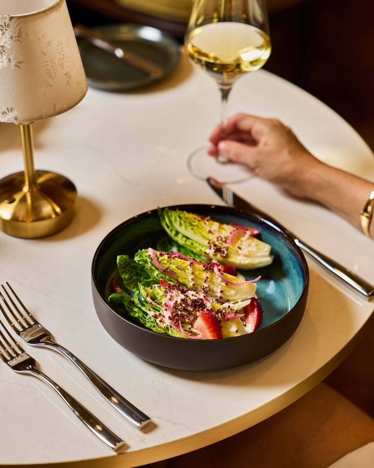 A table setting with a plate of salad, a glass of white wine, and a lamp.