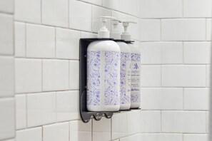 A bathroom with white tiled walls and a black soap dispenser holder holding two bottles of body wash. - Mirbeau Inn & Spa Beacon (Beacon)