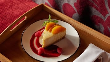 Een stuk cheesecake op een wit bord met rode saus en frambozen, geplaatst op een houten dienblad.
