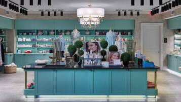 Un hall d’hôtel de charme, avec des meubles de couleur turquoise, un îlot central surmonté d’un lustre, et une variété de produits exposés.