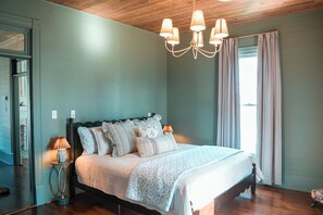 A bedroom with a large bed, a chandelier, and a window with curtains. - Sleeps 22! 3 full kitchens! Downtown Sevierville! Can be used as event space! (Sevierville)
